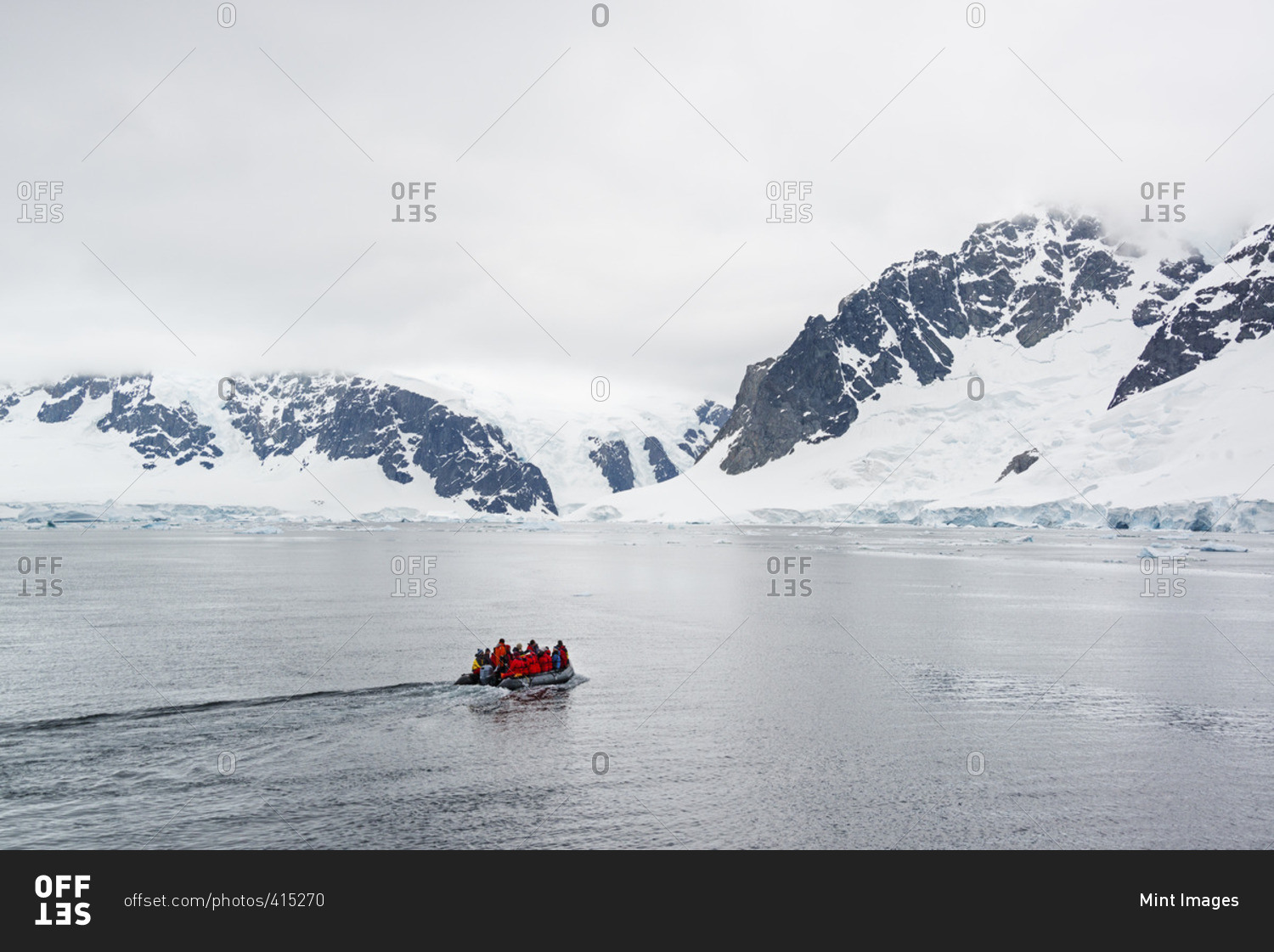 Group of people crossing the ocean in the Antarctic in a rubber boat, snow-covered mountains in the background