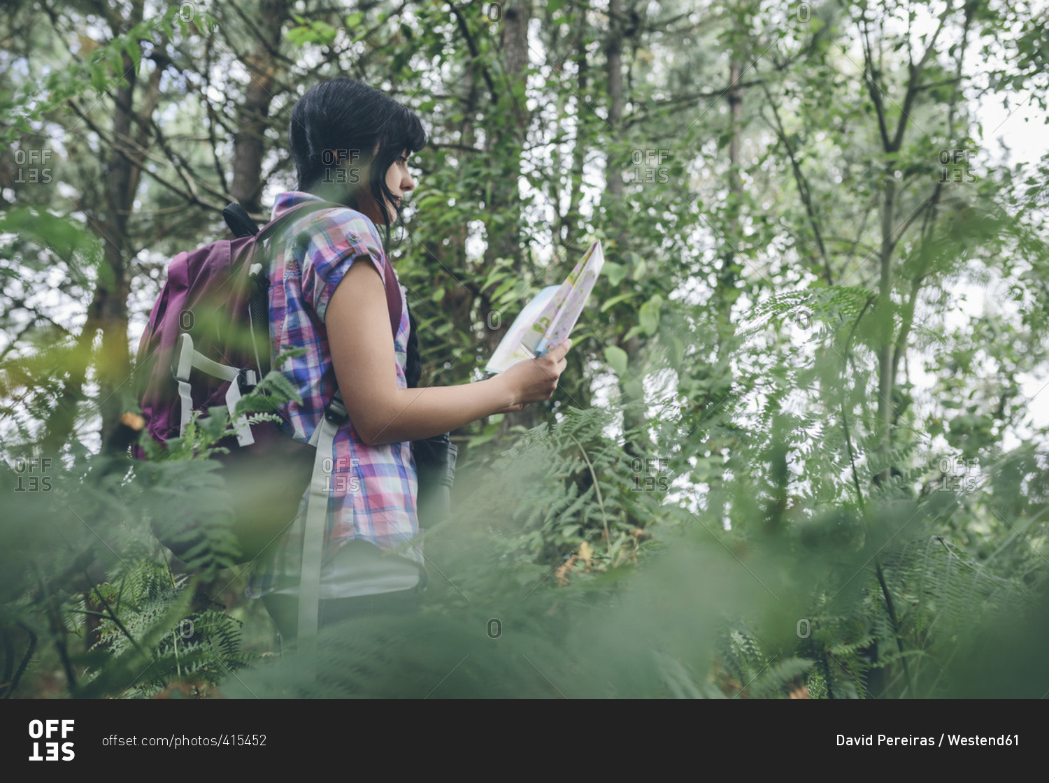 Young woman with backpack looking at hiking map in the forest