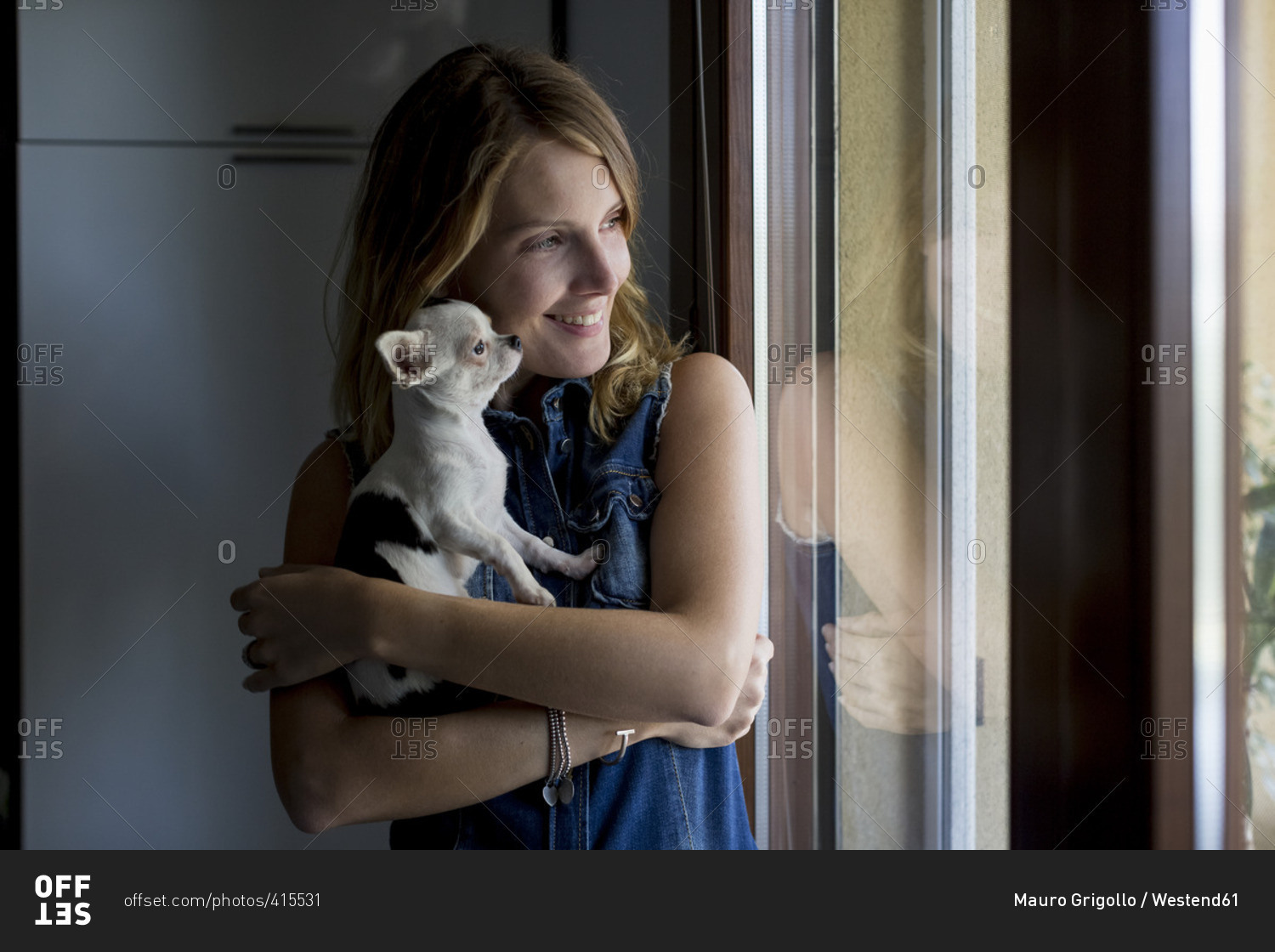 Smiling woman with dog on her arms looking through window