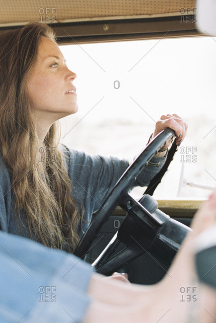 Barefoot woman resting her feet on the dashboard of a 4x4, a tattoo on her right foot, another woman driving
