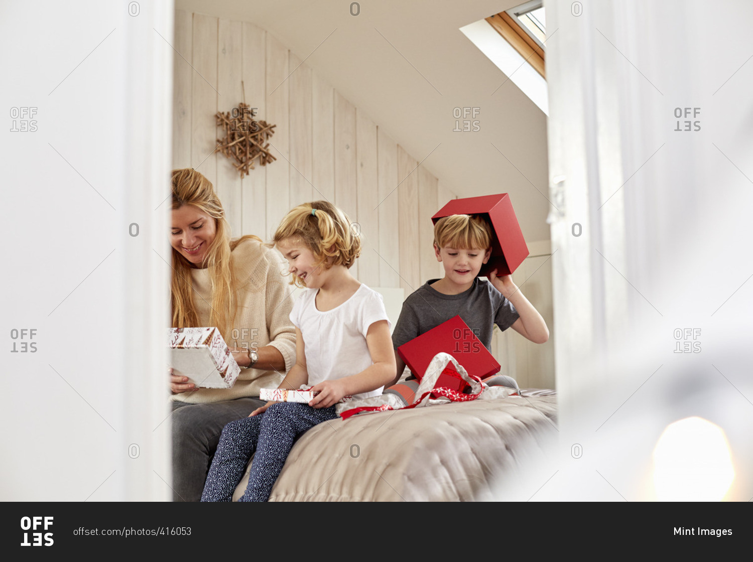 Christmas morning in a family home A mother and two children sitting on a bed opening presents