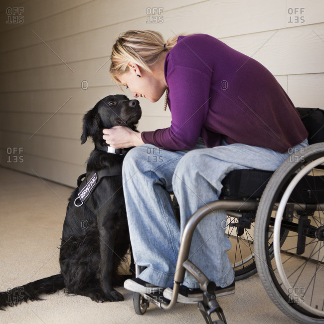 A mature woman wheelchair user stroking her black Labrador service dog and making eye contact with the dog