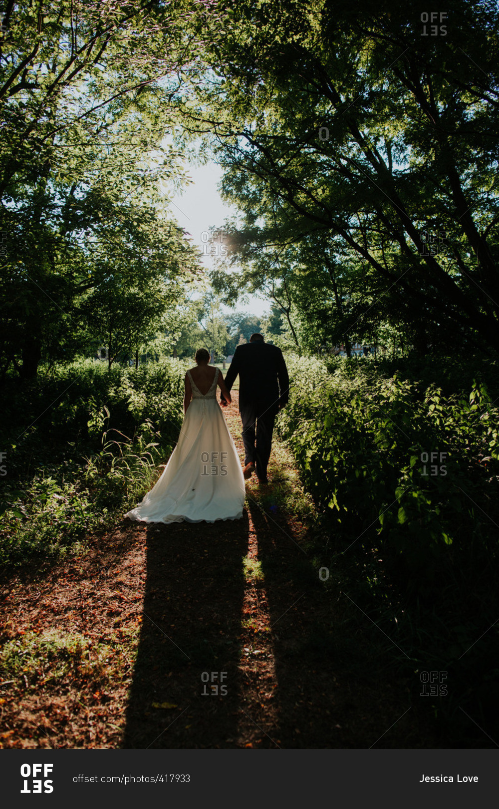 Back view of bride and groom walking on path in woods