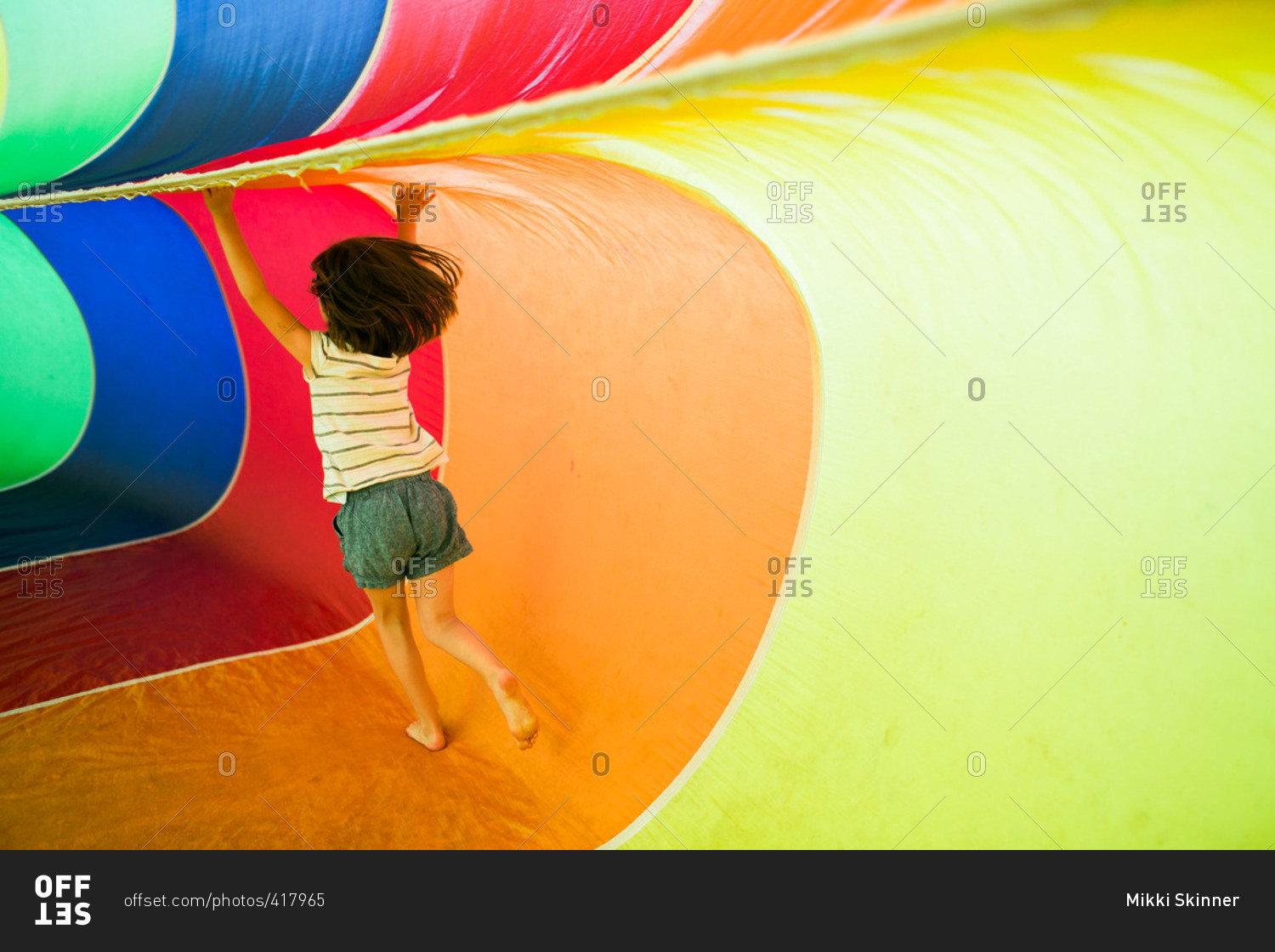 Young girl playing inside a rainbow parachute