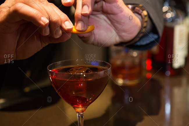 Squeezing oil from orange rind into red cocktail