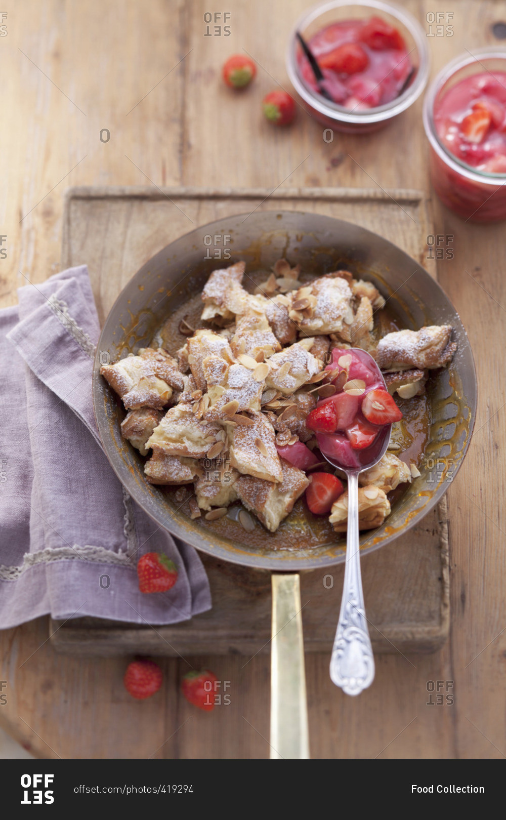 Kaiserschmarrn (shredded sugared pancake from Austria) in a pan with icing sugar, slivered almonds and strawberries, seen from above