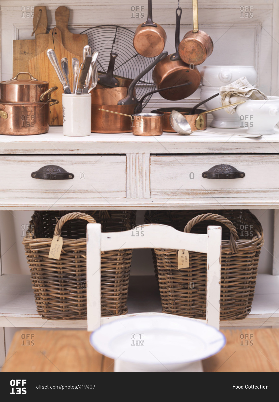 Shiny copper pots on a country house-style kitchen buffet with two large wicker baskets underneath
