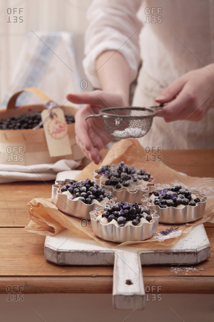 Blueberry tartlets being dusted with icing sugar