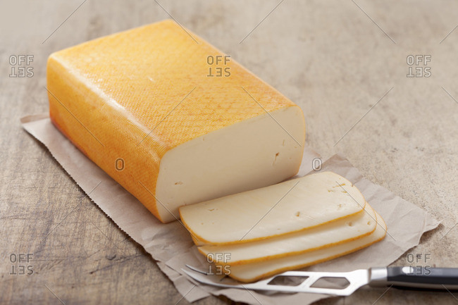 cheese, butter (mild, semi-soft cheese), partly sliced, on paper with a cheese knife