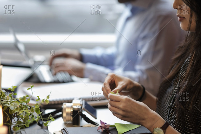 Cropped image of woman making origami while sitting by coworker in creative office
