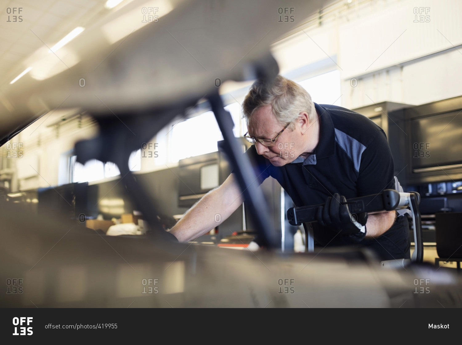 Senior mechanic holding technology while examining car