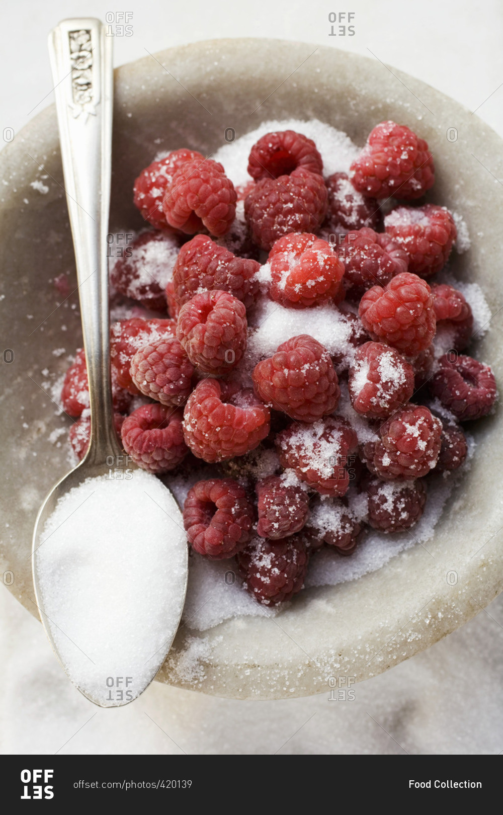 Sugared raspberries in a bowl with a spoonful of sugar