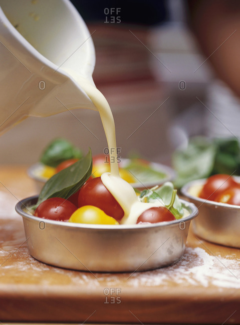 Pouring egg and milk mixture into individual tomato quiche