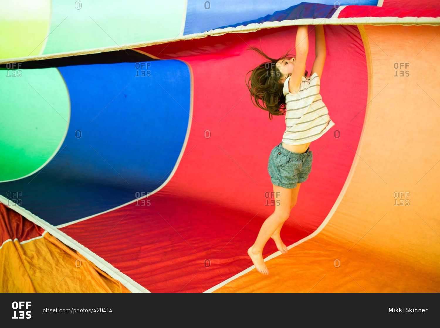 Little girl playing inside a colorful rainbow parachute