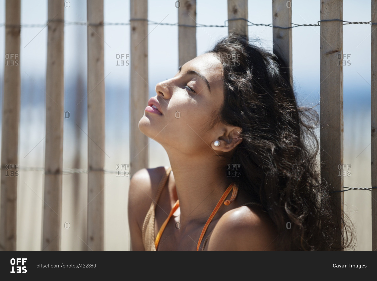Relaxed woman sitting against fence at beach