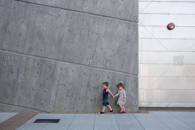 Boy holds sister's hand as they walk outside modern concrete building