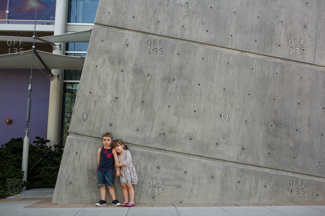 Toddler boy and girl stand against wall outside museum