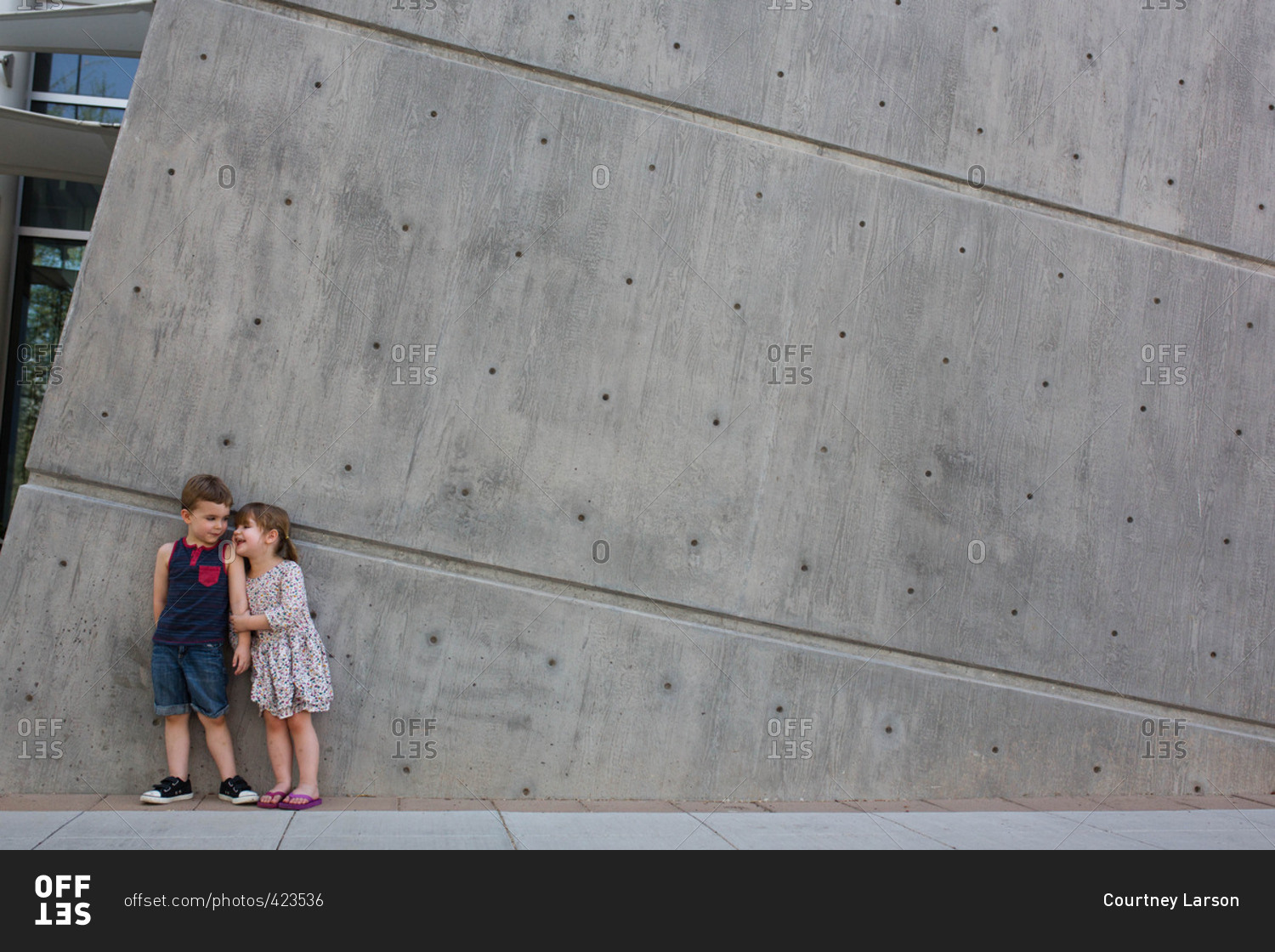 Happy toddler siblings standing against wall outside museum