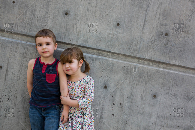 Young brother and sister stand together against cement wall