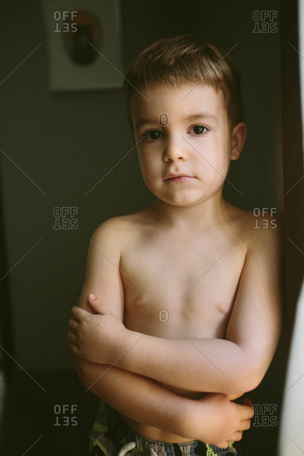 Portrait of a shirtless young boy leaning against a door frame