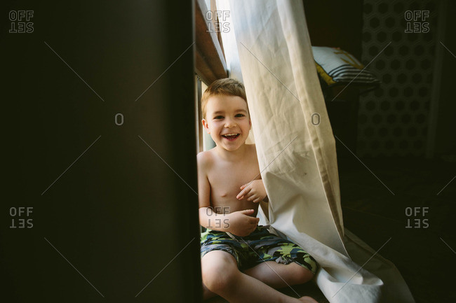 Happy young boy playing behind curtain