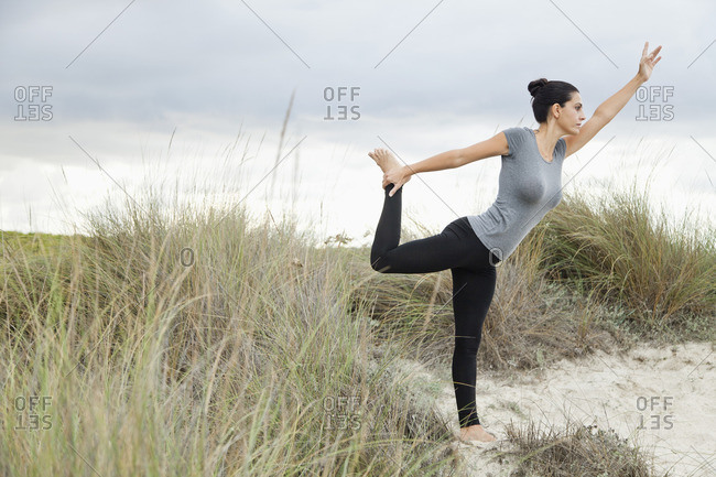 Mature woman in Natarajasana pose on beach, side view