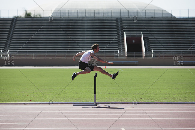 Male athlete clearing hurdle, side view