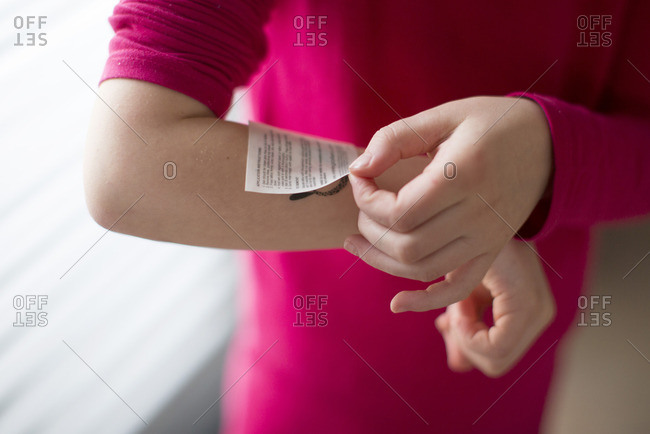 Child applying temporary tattoo to arm, cropped