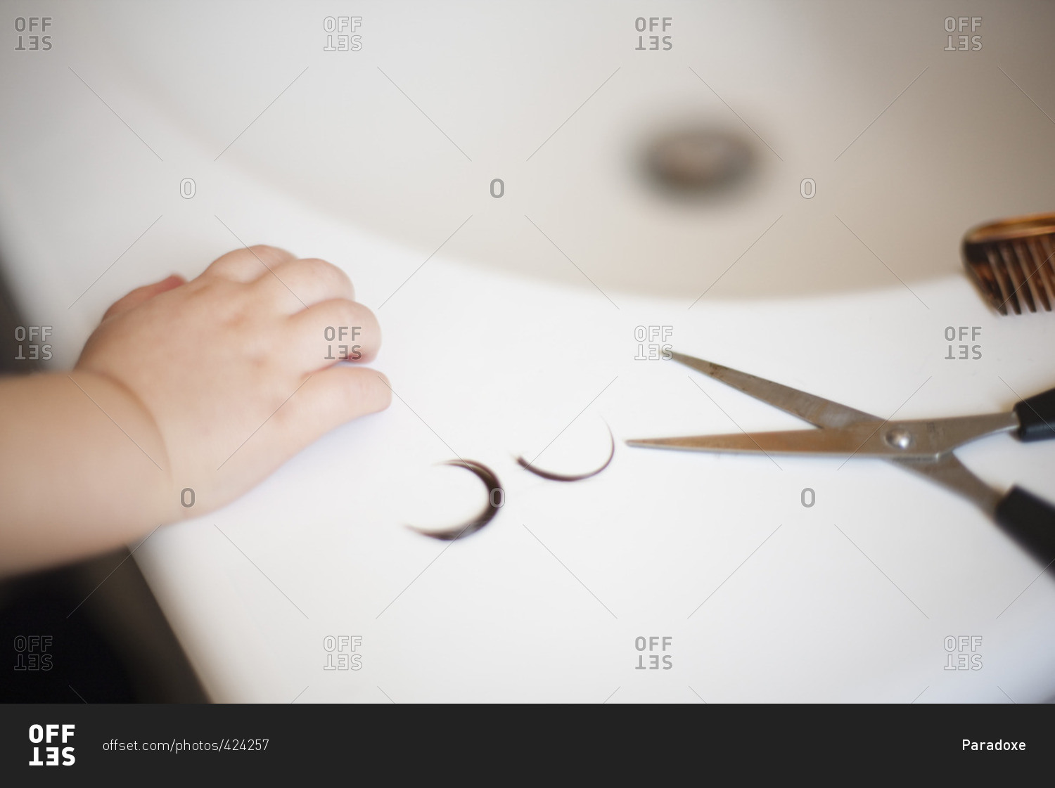 Child's hand resting on sink near scissors and locks of hair