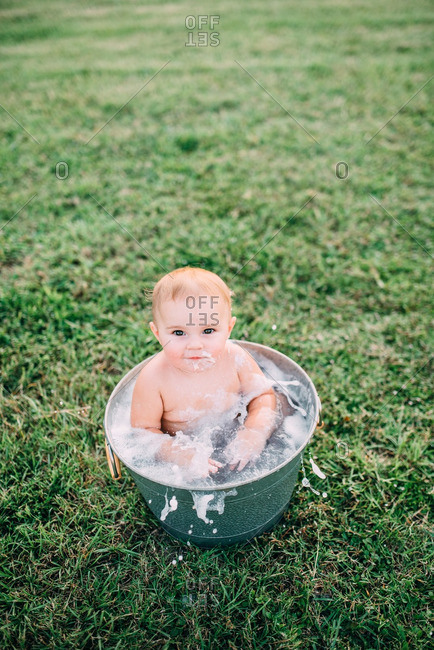 Baby sitting in tub of soapy water on lawn