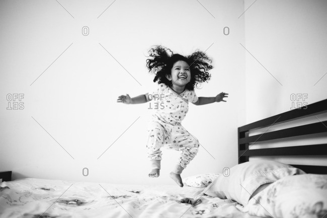 Joyous toddler girl jumping on bed