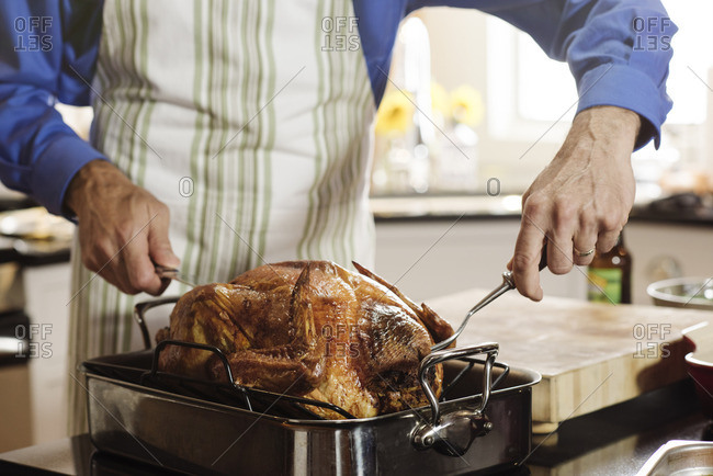 Man removing Thanksgiving turkey from roasting pan to carve