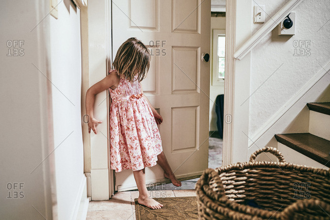 Little girl holding door open with her foot stock photo - OFFSET