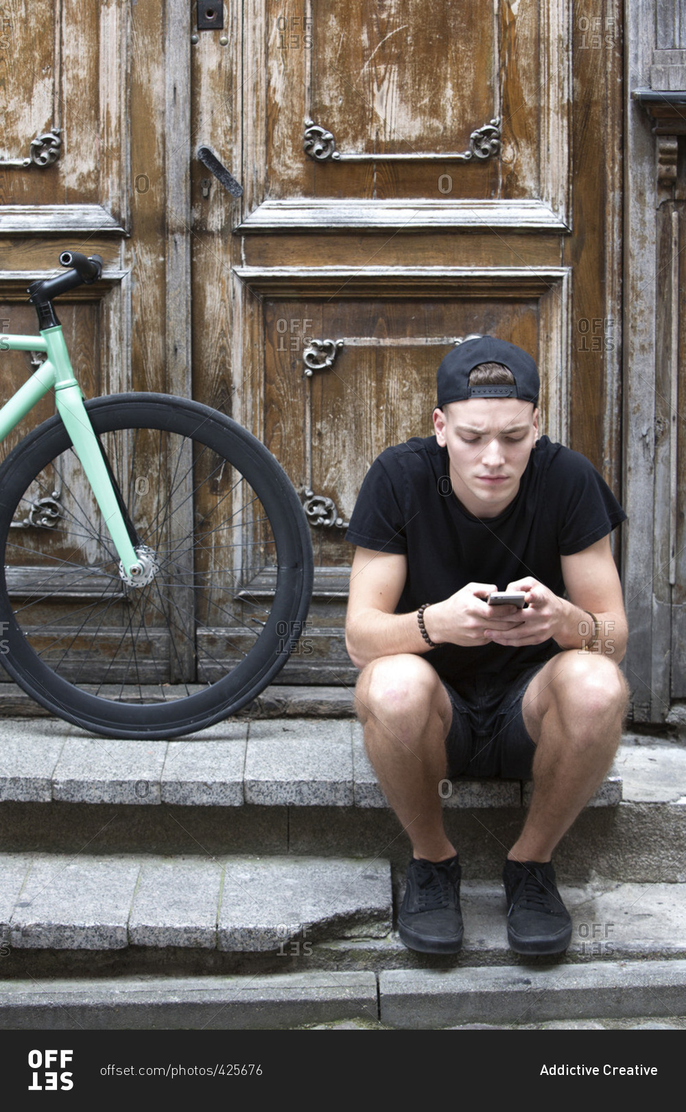 Young man using cell phone on stairs with parked bike at doors