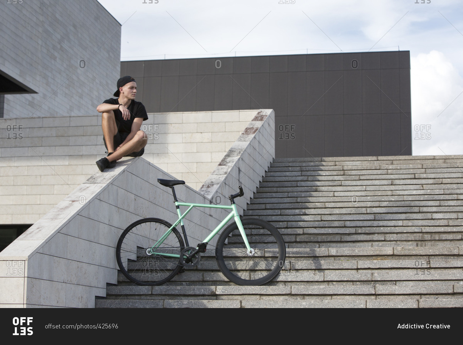 Young boy sitting on stone railing with his bike on stairs
