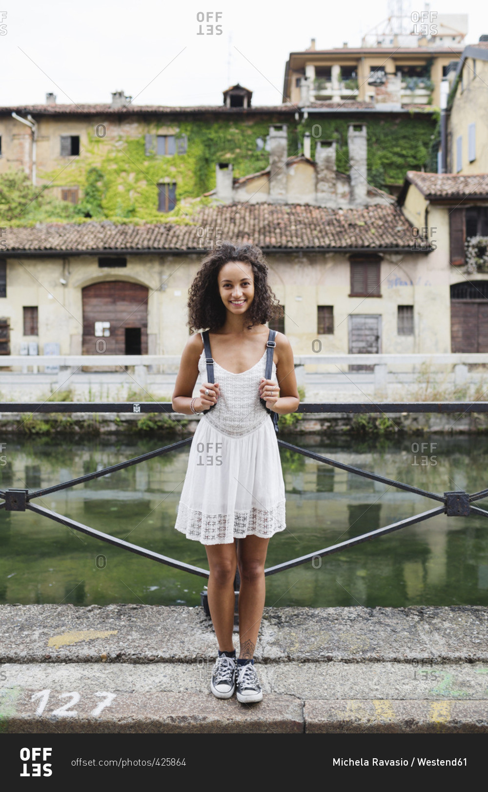 Italy- Milan- portrait of smiling young woman with backpack wearing white summer dress