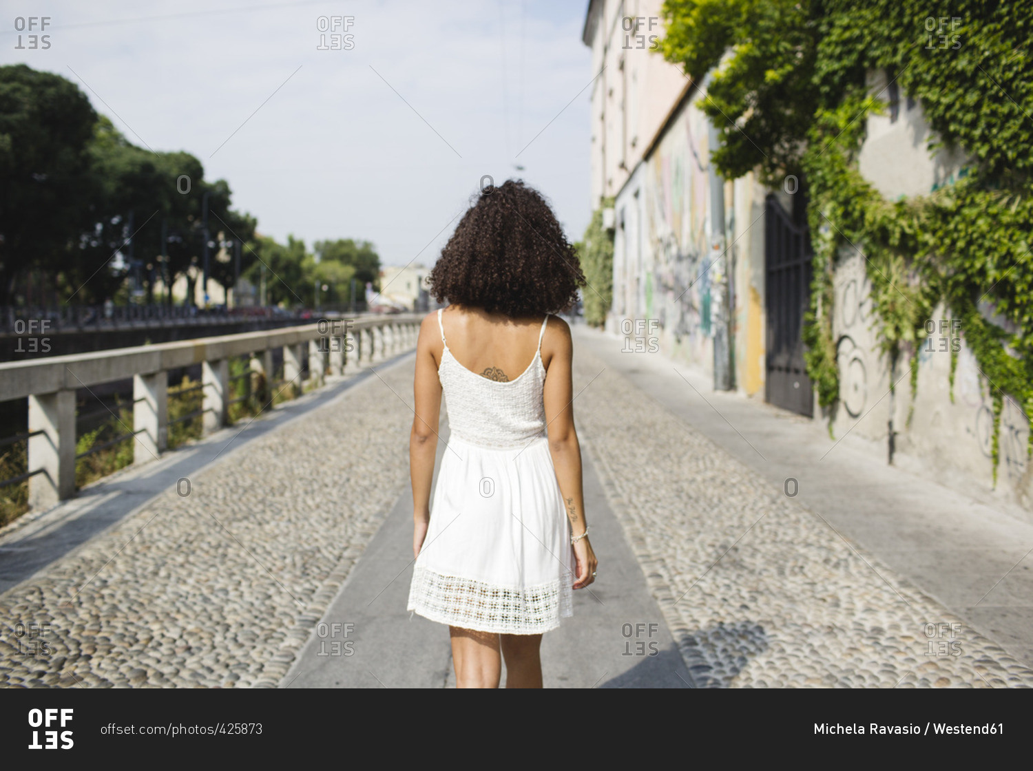 Back view of walking young woman wearing white summer dress