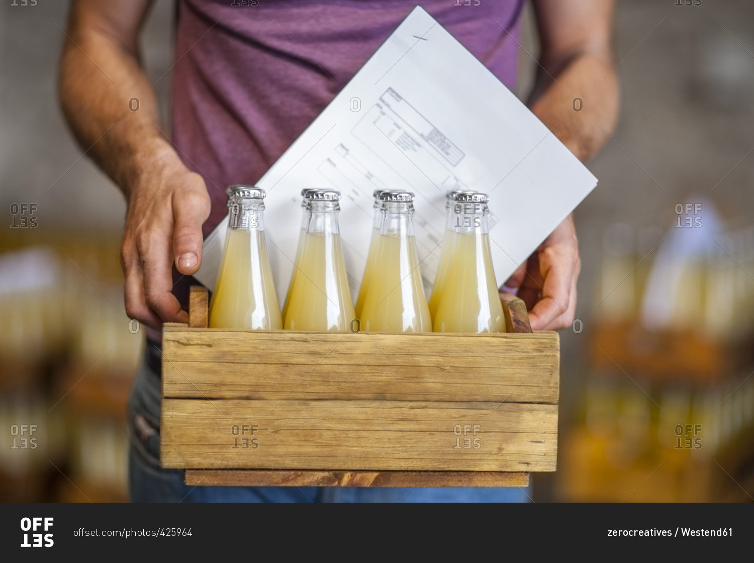 Man carrying wooden box with bottles of juice in warehouse
