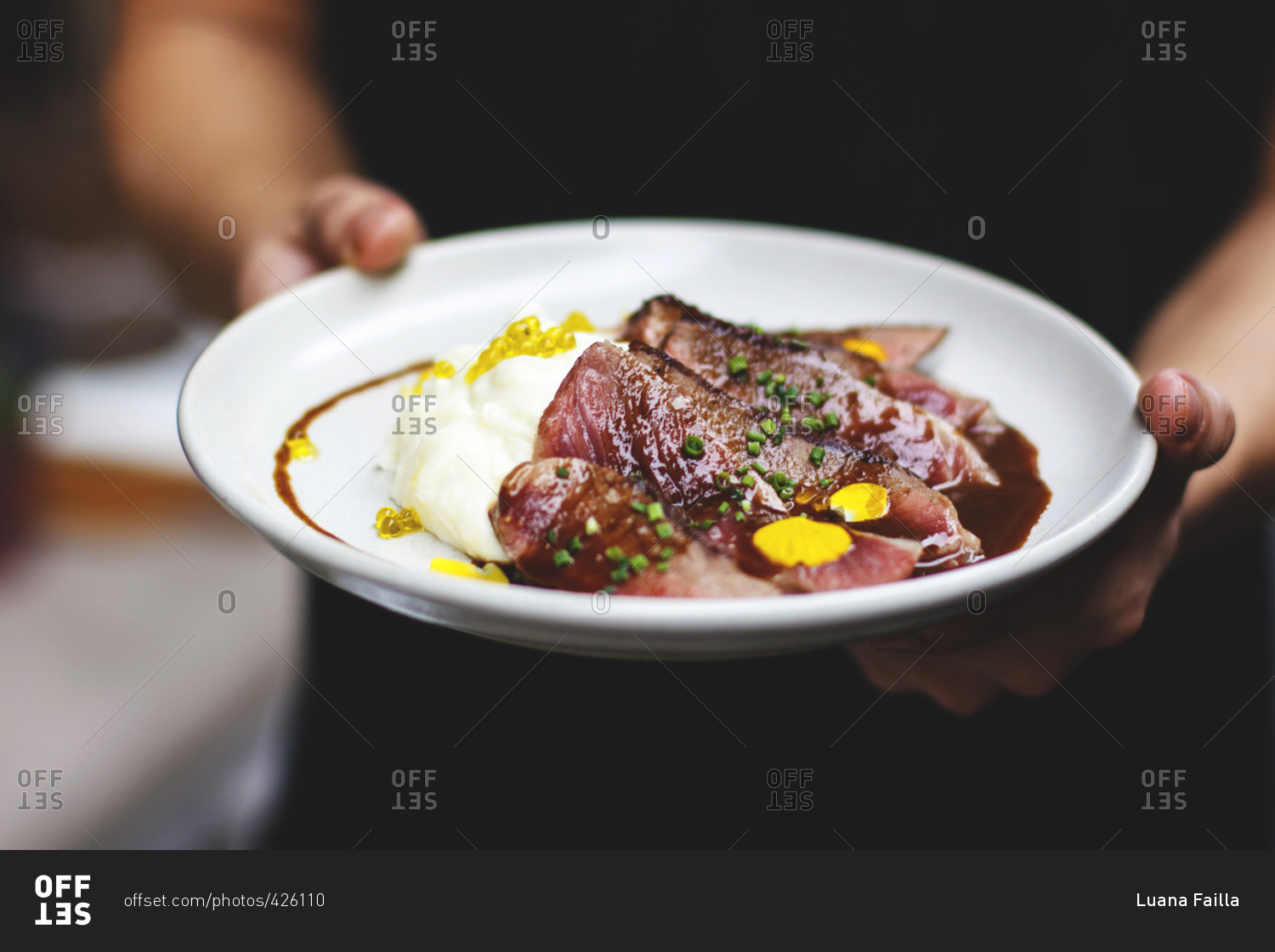 Server holding a plate with sliced rare beef and potatoes