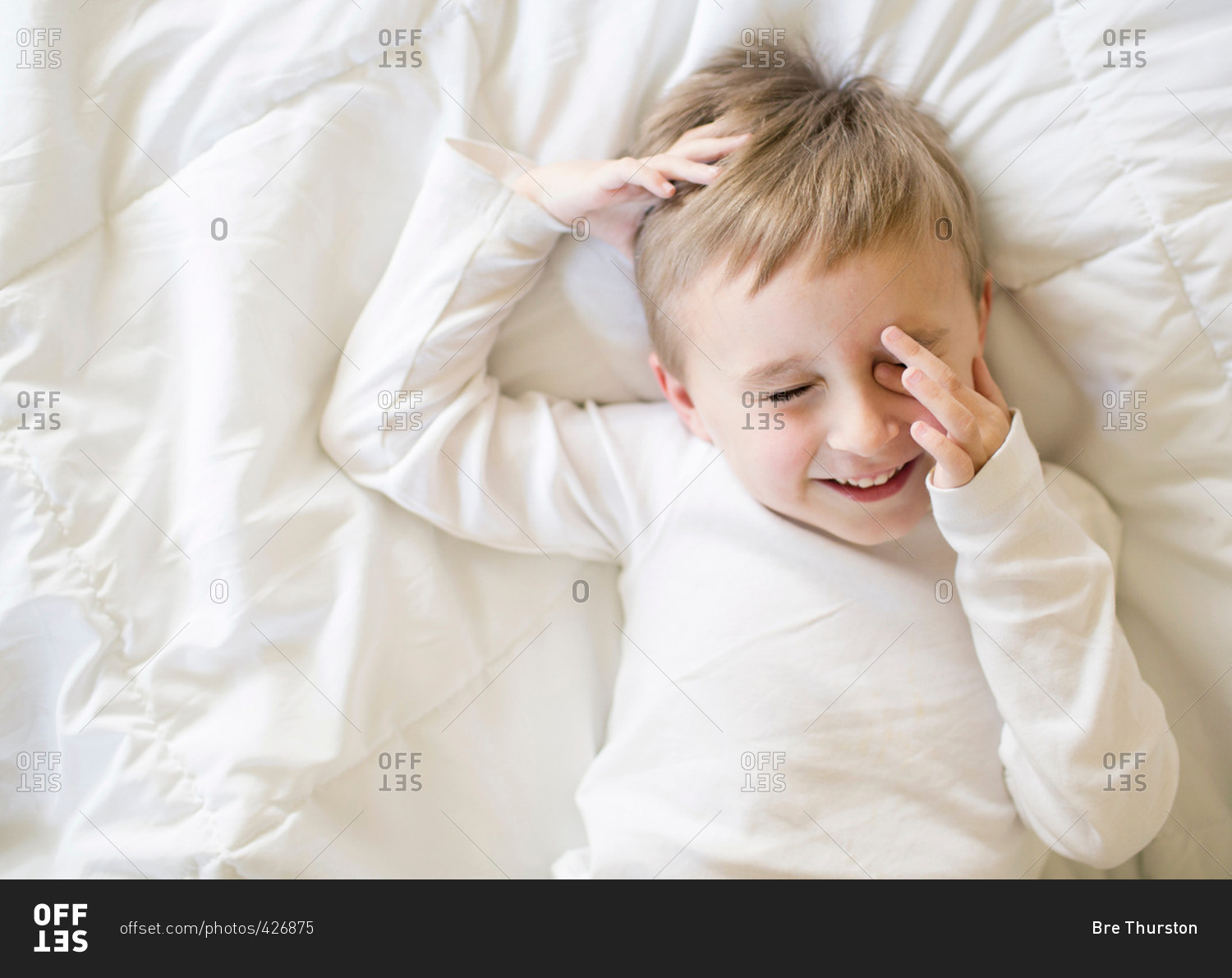 Boy lying on a bed rubbing his eyes and laughing stock photo OFFSET