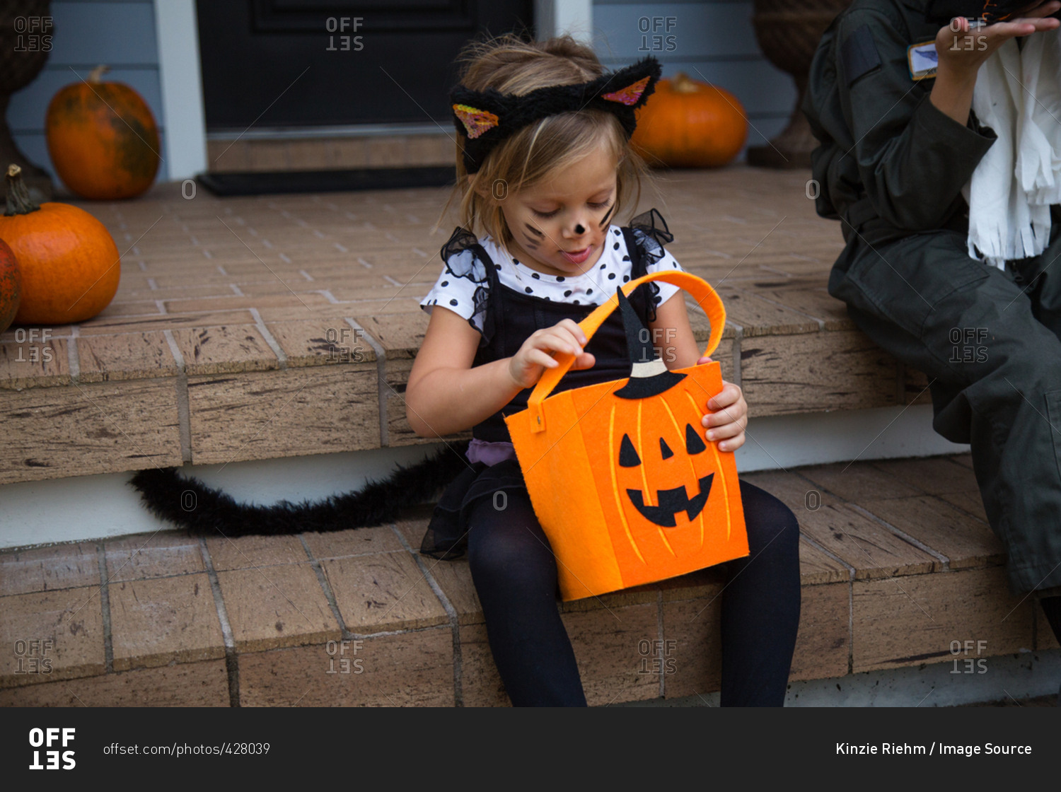 Girl in cat costume peering into trick or treating bag on porch stairway