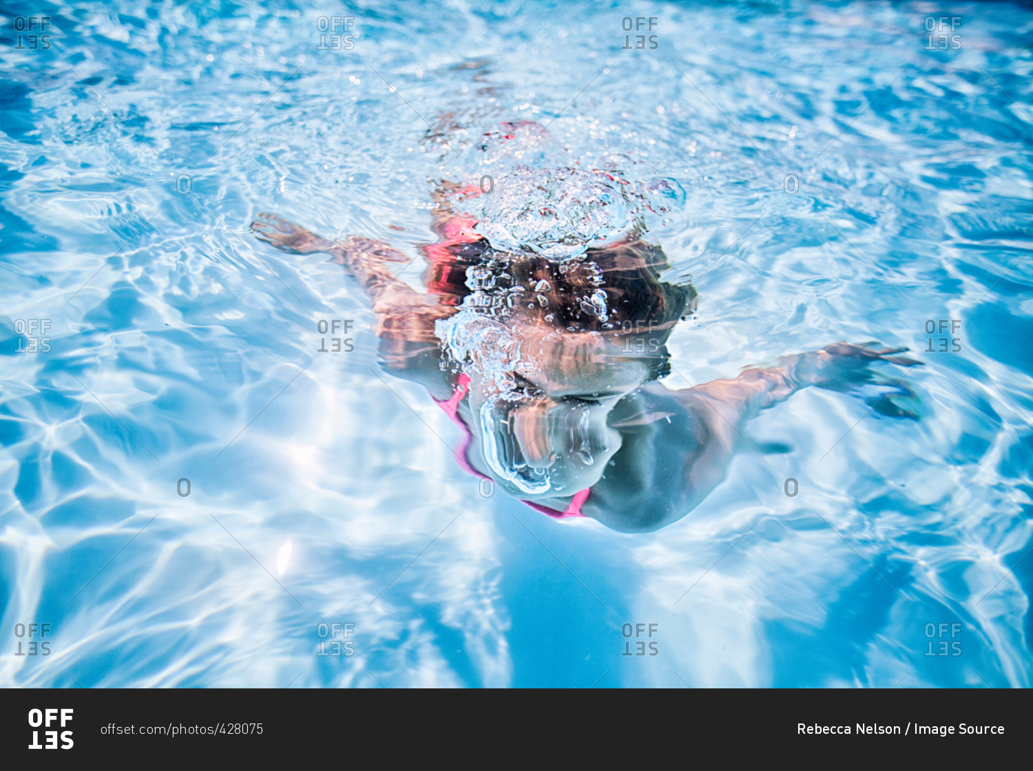 Girl swimming underwater in sunlit swimming pool