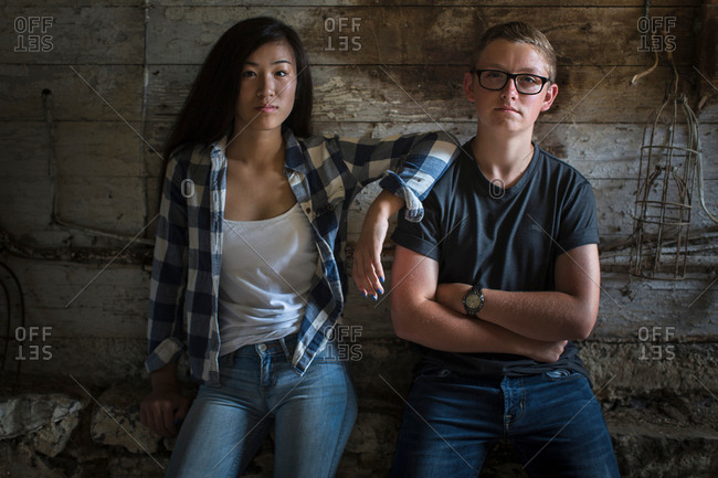 Portrait of sullen teenage couple leaning against dusty shed wall