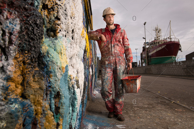 Male ship painter holding paint can leaning against paint splattered wall