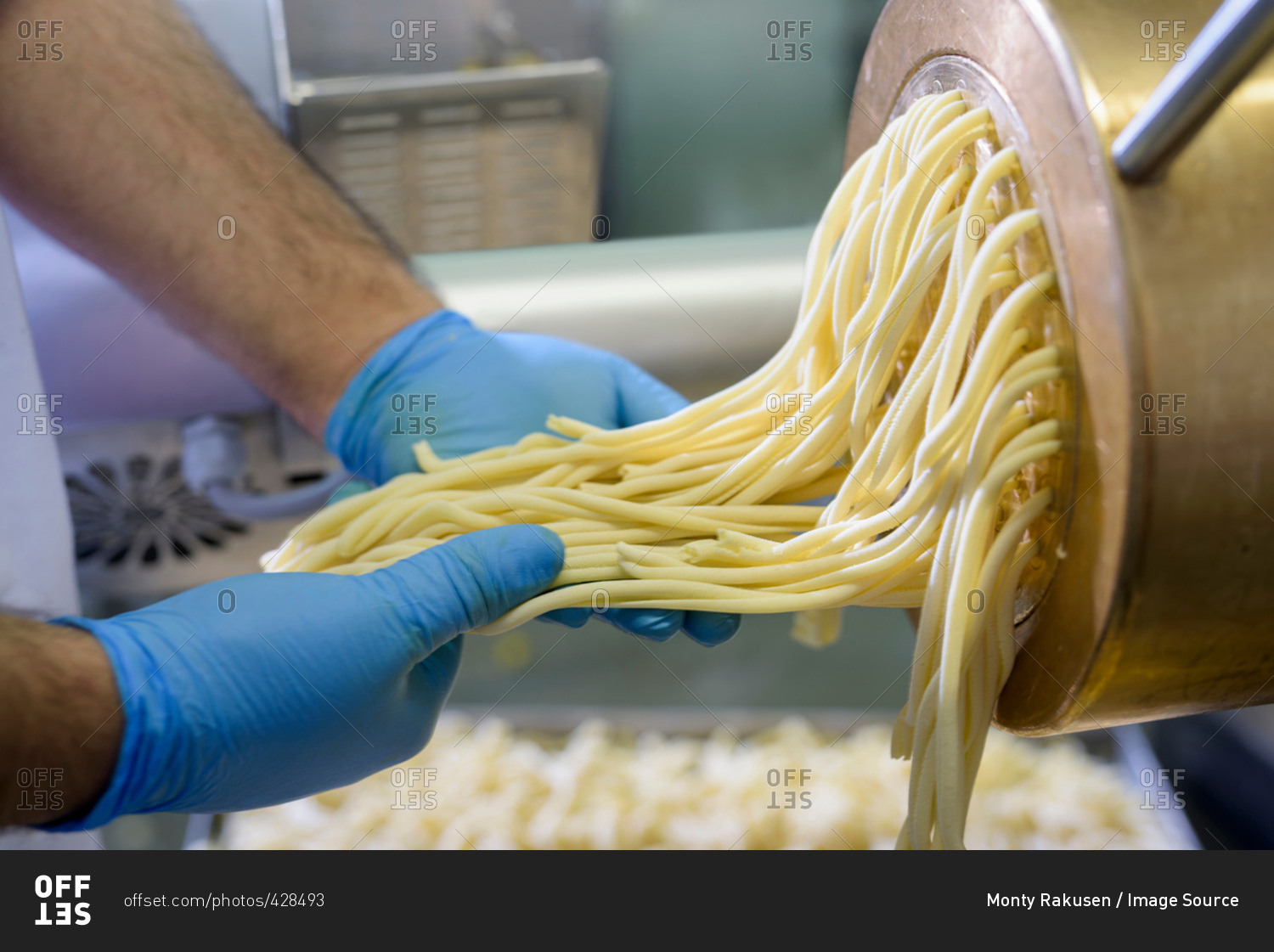 Worker with spaghetti coming out of machine in pasta factory