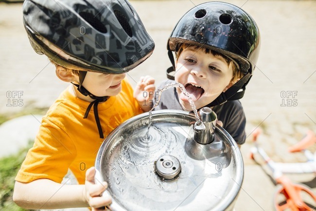 Boys in bike helmets getting drink from water fountain