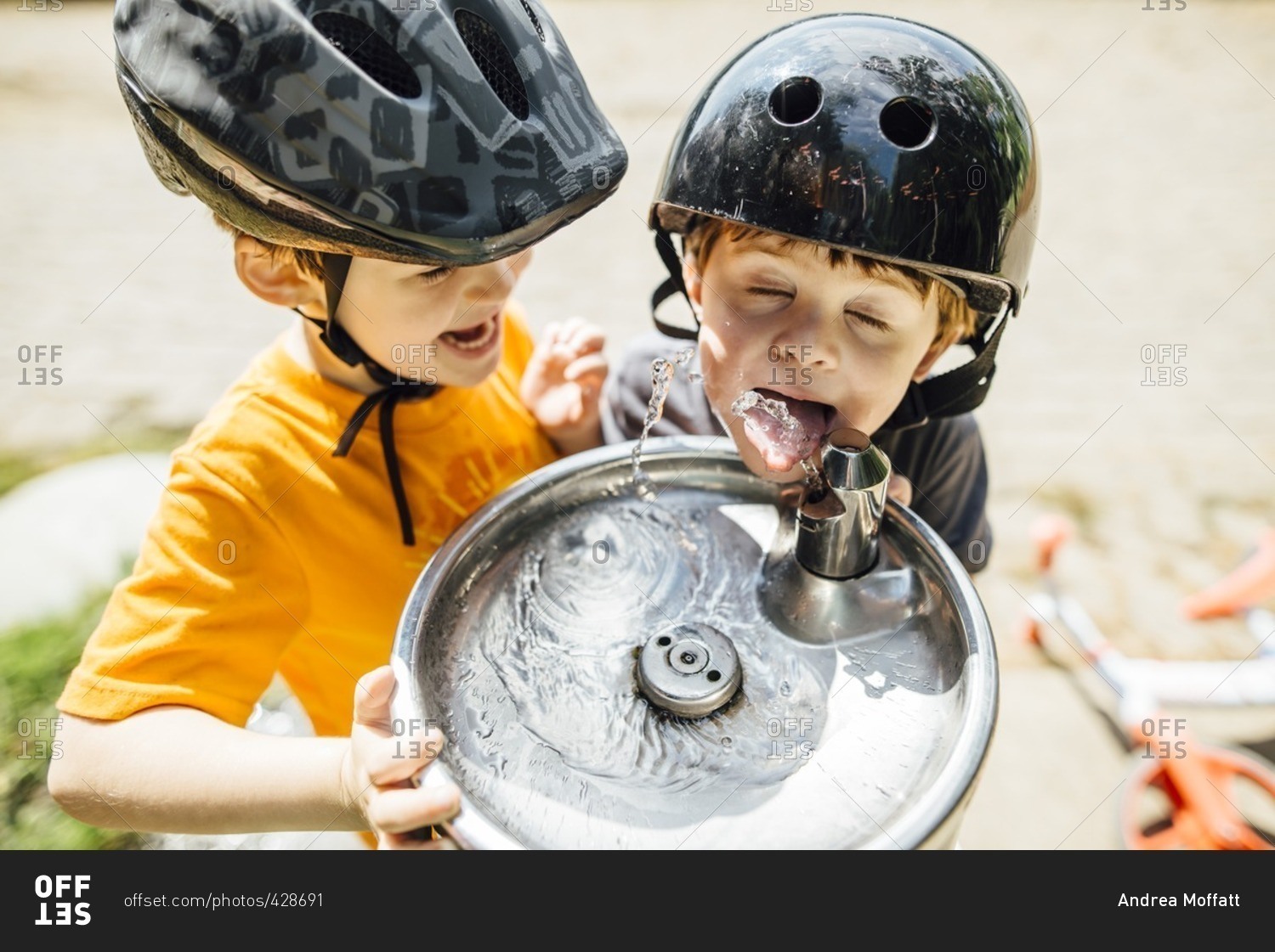 Young boy watches his brother drinking from water fountain
