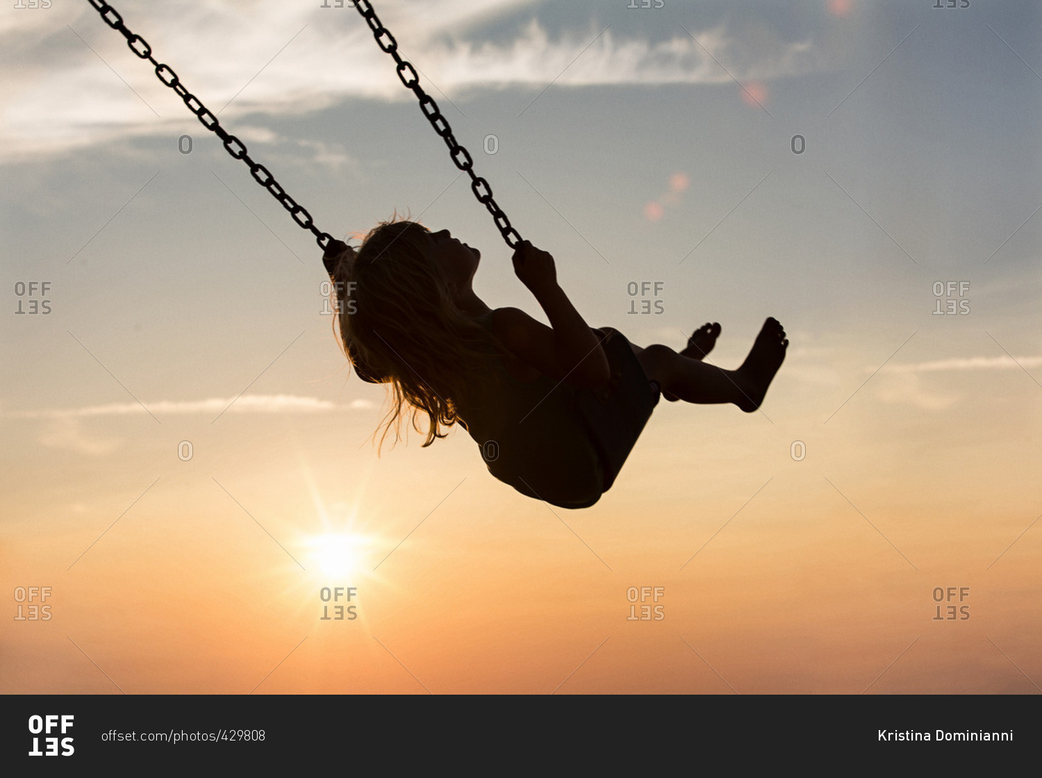Little girl swinging on a swing at sunset