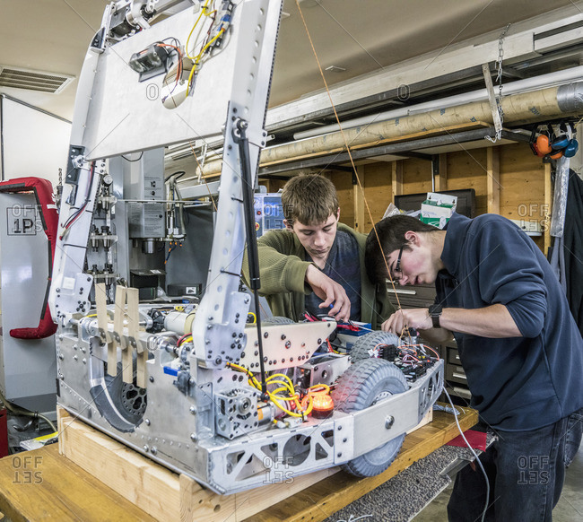 Caucasian robotics students adjusting machinery