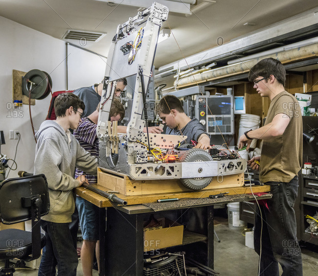 Caucasian robotics students and teacher adjusting machinery